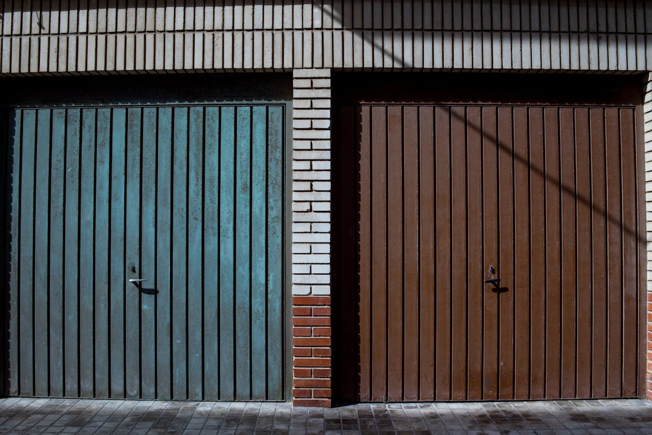 Close-up of side-by-side blue and brown garage doors on a brick facade.